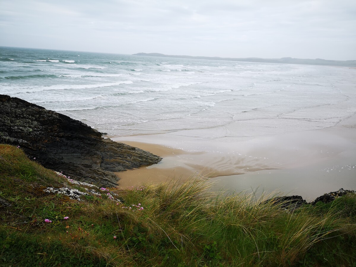 Llun yn dangos traeth gyda thonnau wedi'u gweld o glogwyn