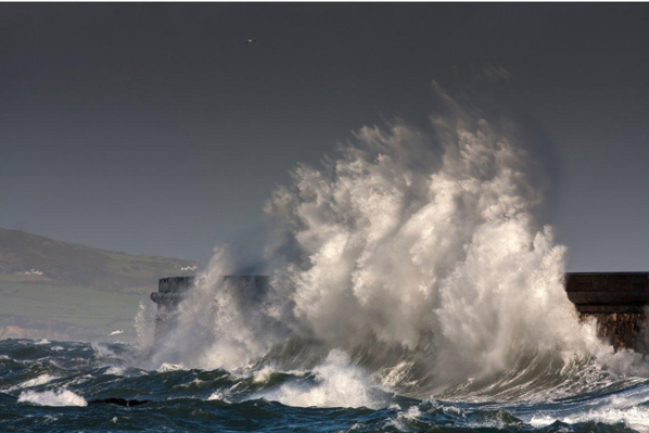 Tonnau'n torri i mewn i wal graig.